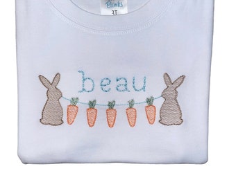 May include: White t-shirt with a blue embroidered bunny rabbit holding carrots and the name "beau" above it.