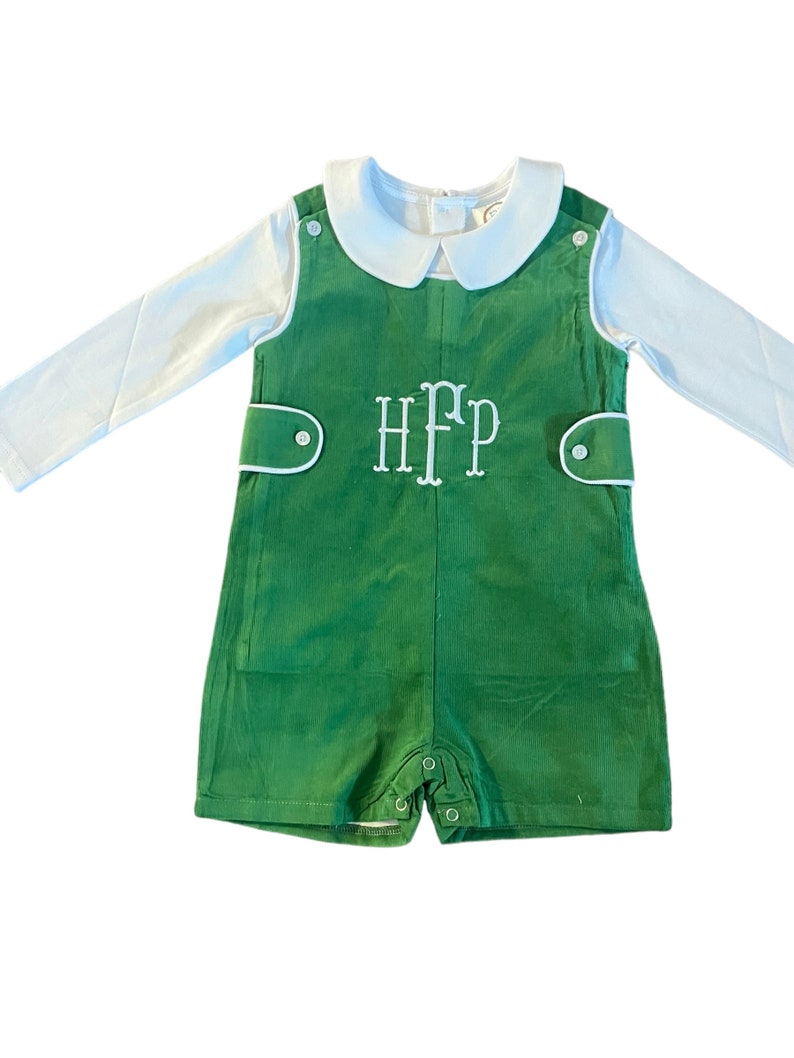 May include: A green romper with white piping and a white long-sleeved shirt. The romper has a white embroidered monogram "HFP" on the front.
