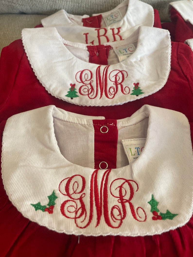 May include: Red corduroy dress with a white Peter Pan collar and a red embroidered monogram with a holly design. The monogram is "SMR".