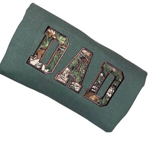 May include: A green sweatshirt with the word "DAD" embroidered in a camouflage pattern.