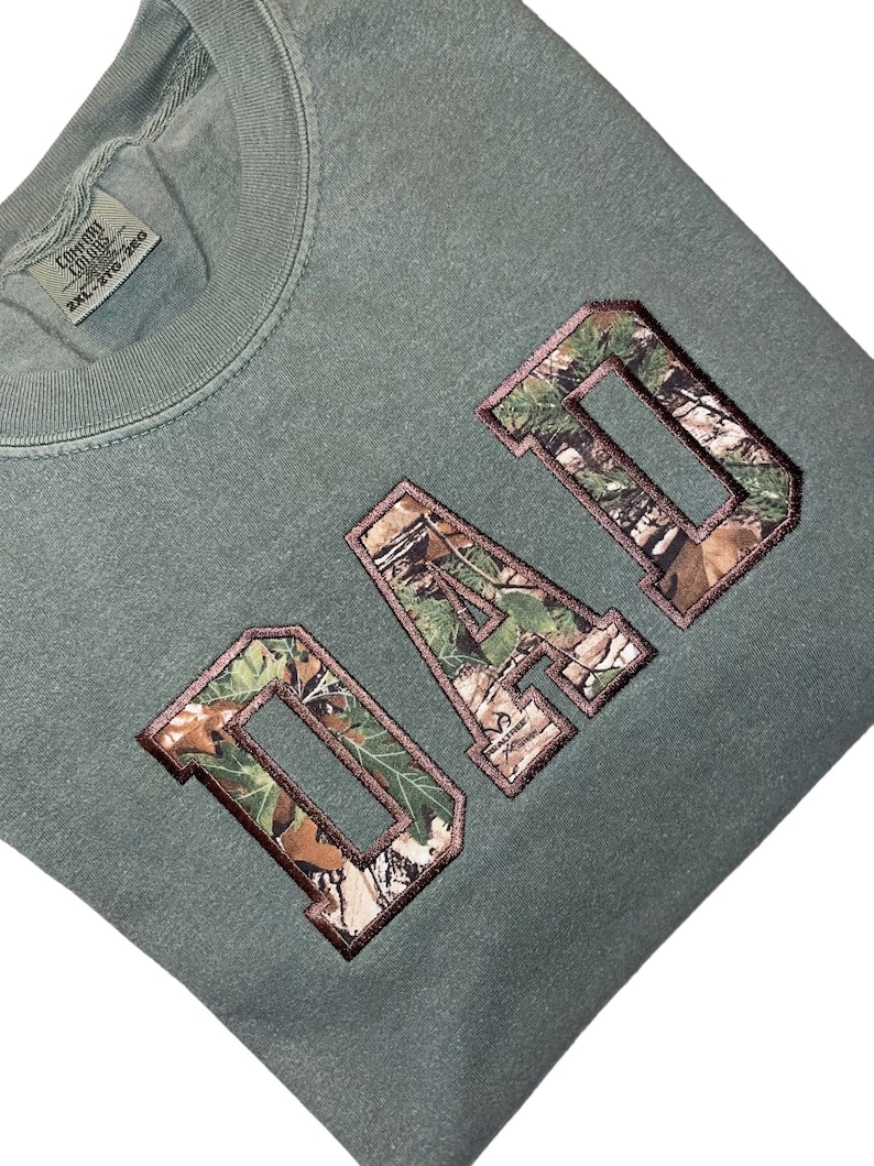 May include: A green sweatshirt with the word "DAD" in large, brown letters with a camouflage pattern inside the letters.