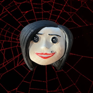 May include: A black and white doll with black hair and a red mouth. The doll is set against a red spiderweb background.