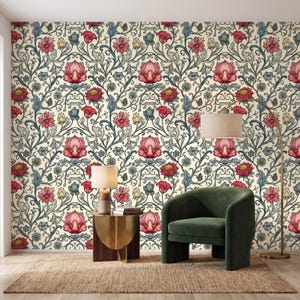 May include: A room with floral wallpaper featuring a repeating pattern of pink and red flowers, green leaves, and blue accents on a cream background. A green armchair, a gold side table, and a floor lamp are in the room.