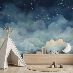 May include: A white fabric teepee stands beside a light wood console table featuring a mural of a dark blue night sky with clouds and gold stars. On the table are books, a gold mobile, a whale plush, and a white crescent moon lamp.
