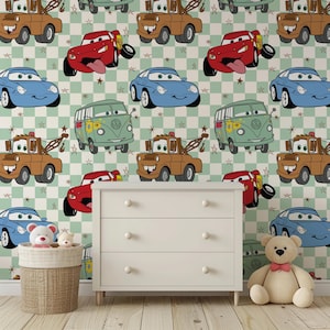 May include: A white three-drawer dresser stands against a wall covered in wallpaper featuring a repeating pattern of cartoon cars from the movie Cars, including red, blue, brown, and green vehicles, on a light green and white checkered background.