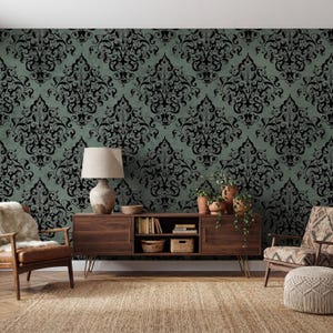 May include: A room with a green damask wallpaper background. A dark wood cabinet with hairpin legs holds books, baskets, and plants. A lamp with a beige shade sits on the cabinet. Two armchairs and a woven rug complete the room's decor.