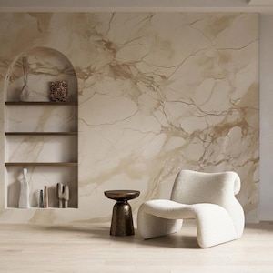 May include: A cream-colored, low-profile armchair with a curved silhouette sits beside a small, dark bronze hourglass-shaped side table. To the left, a recessed arched wall niche features three horizontal shelves holding decorative objects.
