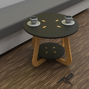 Puede incluir: Una mesa auxiliar negra de dos niveles con un marco de madera. La mesa tiene un diseño geométrico en los niveles superior e inferior. Dos tazas pequeñas están sobre platillos en el nivel superior.