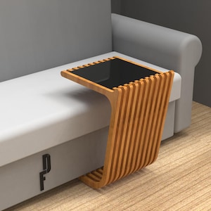 May include: A wooden side table with a black glass top. The table has a unique design with vertical slats and a curved base. The table is next to a grey sofa.