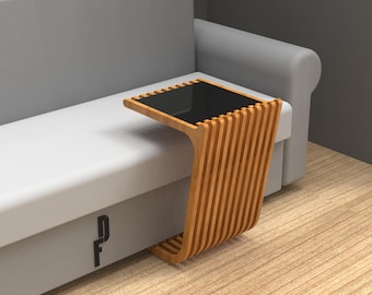 May include: A wooden side table with a black glass top. The table has a unique design with vertical slats and a curved base. The table is next to a gray sofa.