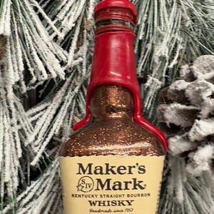 May include: A Maker's Mark whisky bottle ornament with a red wax seal and a label that reads "Maker's Mark Kentucky Straight Bourbon Whisky Handmade since 1953". The bottle is 50 ml and 45% ALC/VOL.