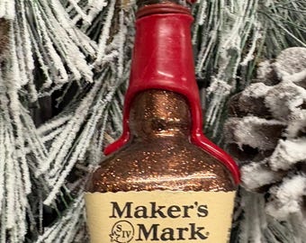 Könnte beinhalten: Ein Weihnachtsornament in Form einer Maker's Mark Whiskyflasche mit rotem Wachssiegel. Das Etikett lautet "Maker's Mark Kentucky Straight Bourbon Whisky Handmade since 1953". Die Flasche ist 50 ml und 45% ALC/VOL.