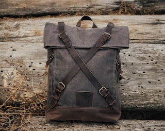 May include: A brown canvas backpack with leather straps and buckles. The backpack has a flap that folds over the top and is secured with a buckle.