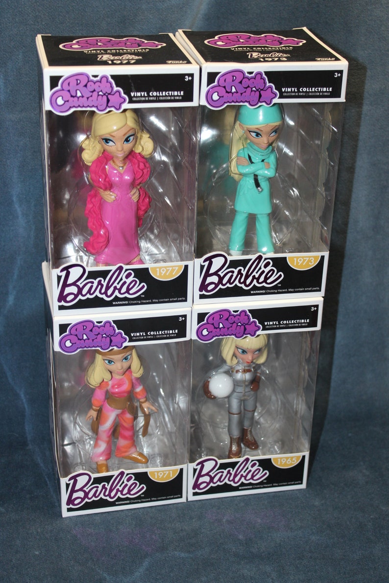 May include: Four collectible vinyl figures of Barbie dolls in different outfits. The dolls are packaged in clear plastic boxes with a pink and purple Rock Candy logo. The boxes have the year the doll was released printed on them: 1977, 1973, 1971, and 1965.
