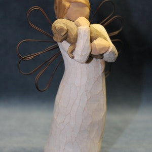 May include: A white wooden figurine of an angel with wings made of wire. The angel is holding a small brown wooden animal in its arms.