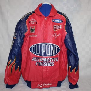 May include: A red and blue racing jacket with multiple sponsor logos, including "DUPONT AUTOMOTIVE FINISHES" and "PEPSI". The jacket features flame designs on the sleeves and the name "Jeff Gordon" on the bottom.