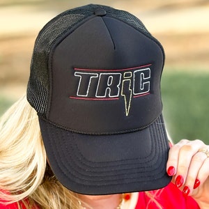 May include: Black trucker hat with a red and white stripe and a yellow lightning bolt. The hat says "TRIC" in white letters.