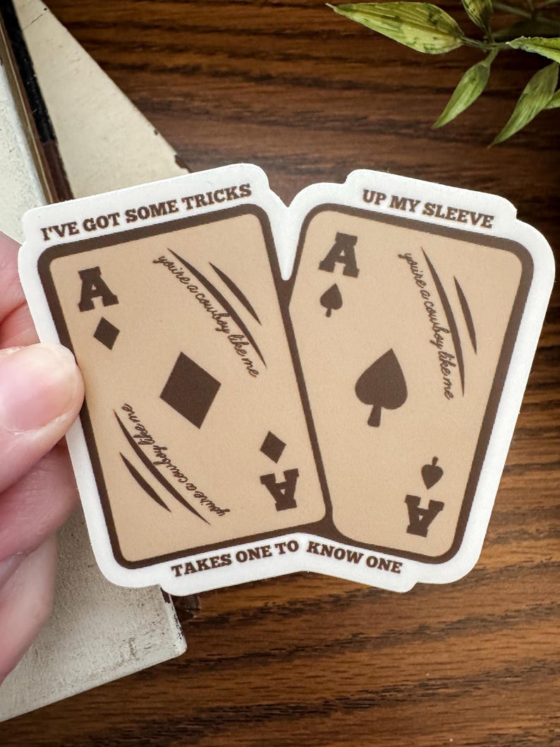 May include: A sticker showing two playing cards, each with an Ace. The cards are tan with brown borders and the text "I've got some tricks" and "Up my sleeve." The phrase "you're a cowboy like me" is also printed on the cards.
