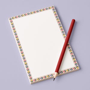 May include: A rectangular notepad with a floral border in yellow, pink, and blue. A red pencil rests diagonally across the notepad. The background is a solid light purple.