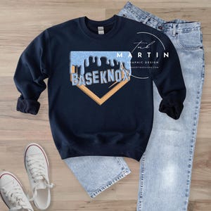 May include: A navy blue sweatshirt with a baseball diamond graphic. The graphic features a blue and white dripping design with the text "BASE KNOW" inside the diamond.