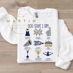 Op de afbeelding: Wit sweatshirt met een marineblauw en gouden ontwerp dat "God zegt dat ik ben" met cheerleading-thema's en bijbelteksten.