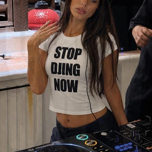 Dj Girl wearing White baby tee with bold STOP DJING NOW slogan print in the dj booth