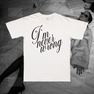 May include: A white t-shirt with the phrase "I'm never wrong" in black cursive script. The shirt is a crew neck style and appears to be made of cotton. The image is a black and white photograph.