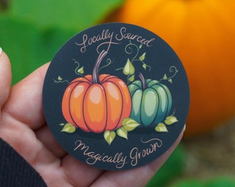 Peut inclure: Un autocollant rond avec un fond bleu foncé représentant deux citrouilles, une orange et une verte, avec des vignes et des feuilles. Le texte "Locally Sourced Magically Grown" est écrit en cursive autour des citrouilles.