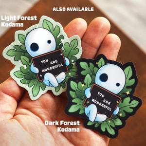 May include: Two sticker designs featuring a white Kodama character holding a sign that says "You are wonderful". The left sticker is a light green forest scene and the right sticker is a dark green forest scene. The text "Also Available" is at the top of the image.