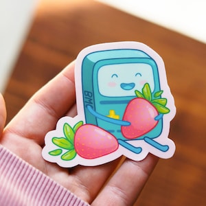 Puede incluir: Un personaje de robot de dibujos animados azul y verde sosteniendo una fresa roja. El robot tiene una cara feliz y el texto "BMC" es visible en el pecho del robot. El robot sostiene una segunda fresa en su otra mano.