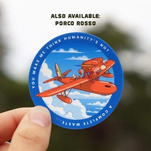 May include: A blue and white circular sticker with a red and white seaplane flying in a blue sky with white clouds. The text on the sticker reads "You make me think humanity's not a complete waste..." and "Also available: Porco Rosso".