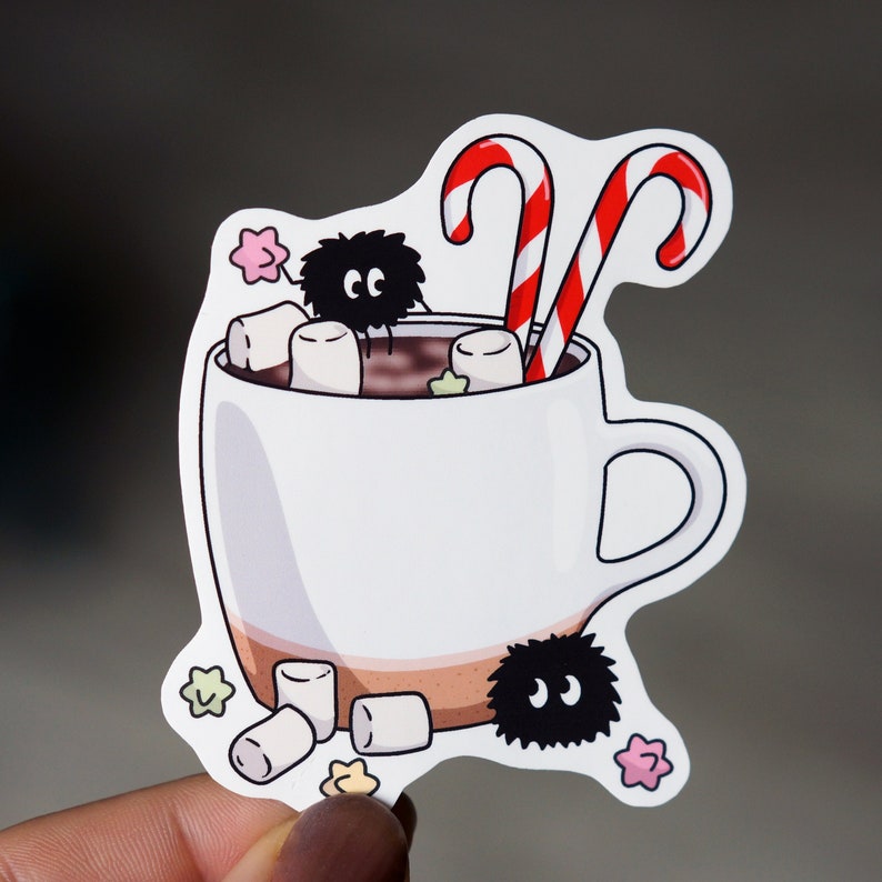 May include: A white mug filled with hot chocolate, topped with marshmallows and two candy canes. Two black and white fuzzy creatures are peeking out from the mug.