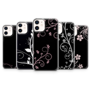 May include: A collection of black phone cases with floral designs. The cases feature various patterns of white and pink flowers, vines, and swirls. The cases are shown in a row, each with a different design.