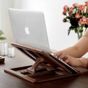 May include: A wooden laptop stand with a personalized inscription "Cyrus Ellman". The stand is made of dark wood and has a natural finish. It is designed to elevate a laptop to a comfortable viewing angle.