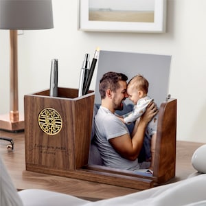 May include: Wooden desk organizer with a photo frame, a pen holder, and a decorative design. The photo frame shows a father and son smiling at each other. The organizer has the text "I love you papa 6.16.2024" engraved on the front.