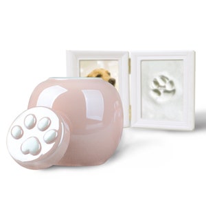 Pu&ograve; includere: Urna per animali domestici in ceramica rosa con un coperchio a forma di impronta di zampa. L'urna &egrave; accanto a una cornice bianca con un'impronta di zampa nella foto.