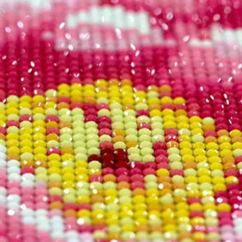 May include: Close-up of a diamond painting with small, colourful, square-shaped rhinestones. The rhinestones are arranged in a pattern of pink, yellow, and white.