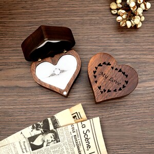 May include: A wooden heart-shaped ring box with a hinged lid. The box is open and a ring is inside. The box is engraved with the words "My Love" and a design of hearts.