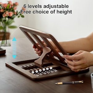 May include: A wooden book stand with six adjustable levels, allowing for a variety of viewing angles. The stand is made of dark brown wood and has a smooth finish. The stand is shown in the image with a pen on a wooden table. The stand has six levels of adjustment, with the angles marked in degrees: 18&deg;, 26&deg;, 34&deg;, 42&deg;, 50&deg;, and 58&deg;.