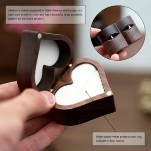 May include: A heart-shaped wooden ring box with a velvet interior. The box is made of walnut wood and has a dark brown color. The box is open and the velvet interior is visible. The text "High-quality velvet protects your ring, available in four colors" is visible below the box.