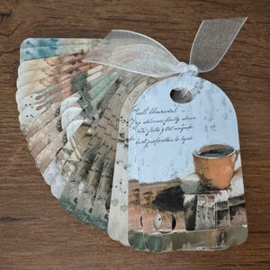 May include: A set of decorative paper tags tied with a sheer ribbon. The tags feature a watercolor design with a coffee cup illustration and handwritten text. The tags are arranged in a fan shape, showcasing a vintage aesthetic.