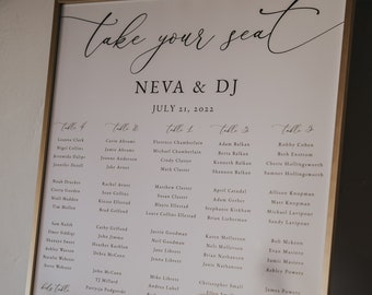 Op de afbeelding: Een wit zitplan met een gouden lijst, met de namen van de gasten voor een huwelijksreceptie. Het plan is getiteld "Take Your Seat" met de namen van het paar "Neva & DJ" en de datum "July 21, 2022".