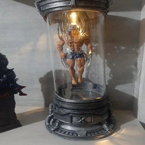 Könnte beinhalten: Ein silberner und schwarzer Präsentationsständer mit einem Glaszylinder, der eine detaillierte Actionfigur eines Superhelden mit Krallen enthält. Die Figur schwebt in der Luft mit Drähten, die an ihrem Körper befestigt sind. Die Basis des Ständers hat ein X.
