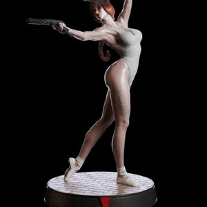 May include: A white figurine of a woman in a white leotard holding two guns, standing on a black base with a red widow symbol.