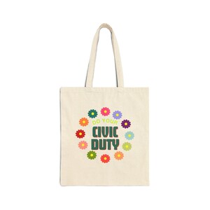May include: A beige tote bag with a green, white, and yellow design. The design features a circle of colorful flowers with the text "Do Your Civic Duty" in the center.
