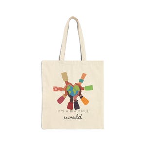 May include: A beige tote bag with a colorful illustration of hands holding a globe. The text "It's a beautiful world" is printed below the image.