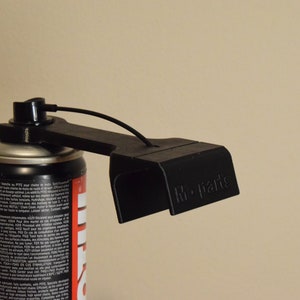 以下が含まれることがあります： 黒色の3Dプリントされたスプレー缶ホルダーで、上部に黒いコードが取り付けられています。ホルダーは、黒と赤のテキストが書かれた銀色のスプレー缶に取り付けられています。ホルダーには、側面に「M-Parts」というテキストが印刷されています。