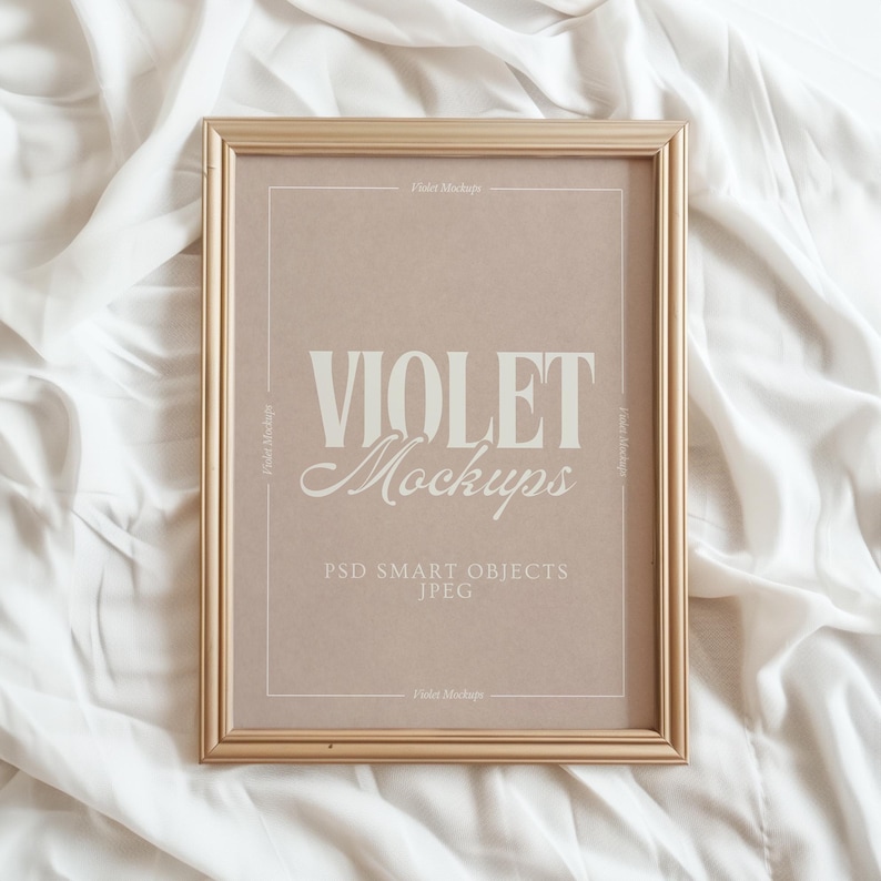 May include: A gold rectangular frame displaying the text "VIOLET Mockups" in a serif font. The frame is set against a light brown backdrop with the text "PSD SMART OBJECTS JPEG". The background is a white, textured fabric.