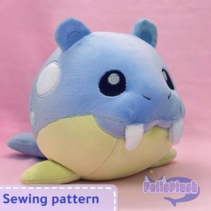 Pode incluir: Um brinquedo de pelúcia em forma de morsa de desenho animado, principalmente azul com barriga amarela e presas brancas. O brinquedo tem um corpo redondo, orelhas pequenas e uma expressão sorridente. O texto "Sewing pattern" é visível.