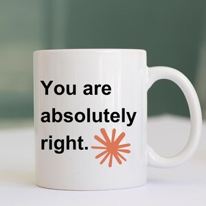 May include: A white ceramic mug featuring the black text "You are absolutely right." printed on the front, accompanied by a small, orange, multi-pointed starburst graphic positioned to the right of the final word of the sentence.
